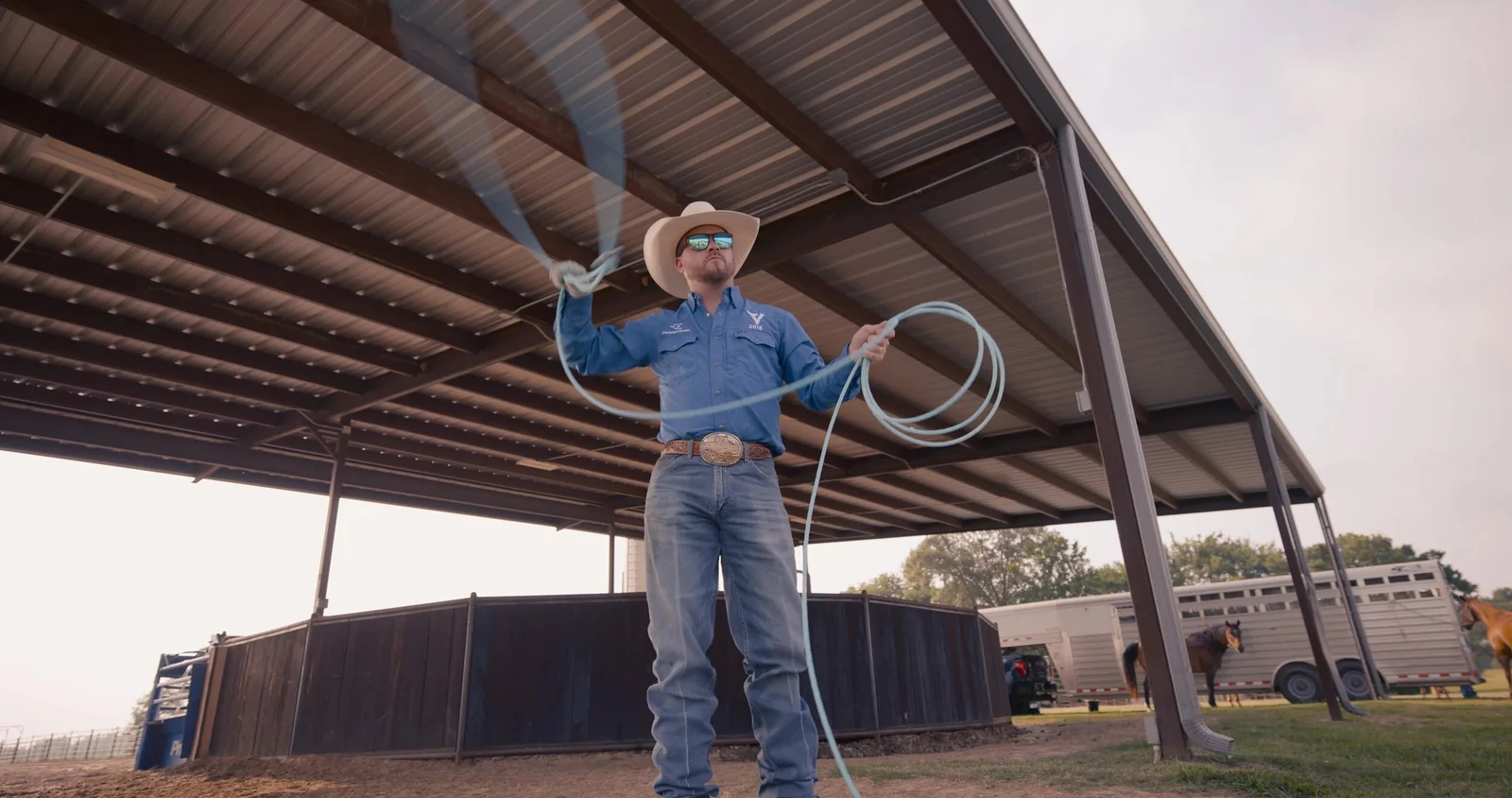 A cowboy swinging a rope beneath a covered arena